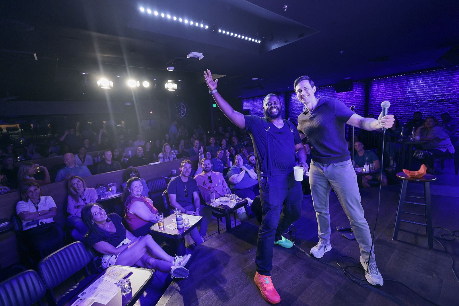 Corey Martin Craig on stage with a comedian in front of a full comedy club crowd